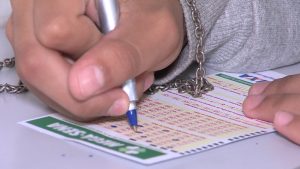 Imagem de uma pessoa segurando uma caneta e preenchendo números em uma cartela de jogo da mega da virada