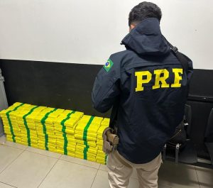 Policial Rodoviário Federal à frente de uma pilha de maconha apreendida