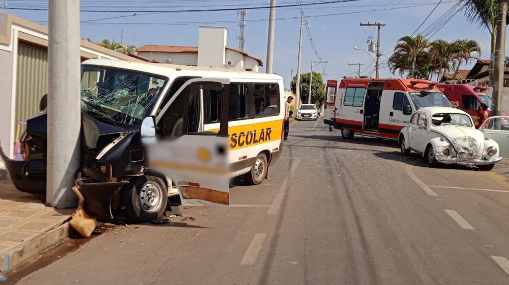 Van escolar batida em poste e ambulância ao fundo