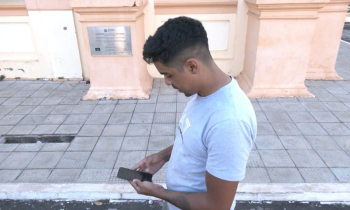 Lázaro de Souza Oliveira segurando celular e olhando para baixo, na tela