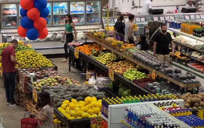 Um supermercado com diversos produtos e alimentos expostos, além dos clientes andando pelo estabelecimento