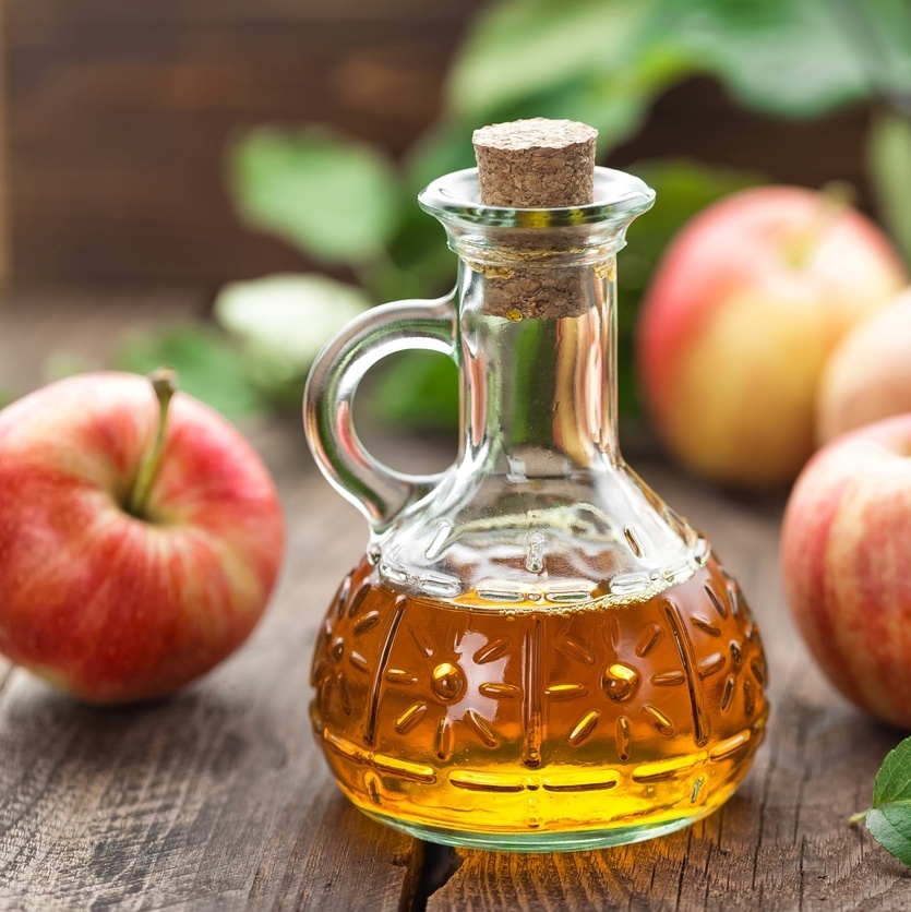 Frasco com vinagre de maçã em cima de uma mesa com frutos de maçã ao lado