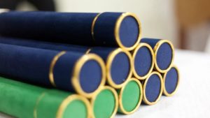 Mesa com dez canudos de formatura em cima, de cores azuis e verde