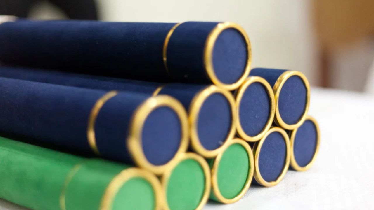Mesa com dez canudos de formatura em cima, de cores azuis e verde