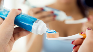 Escova de dentes com cerdas brancas e azuis aparece com uma porção de creme dental branco aplicado. Colgate anuncia descontinuamento de creme dental.