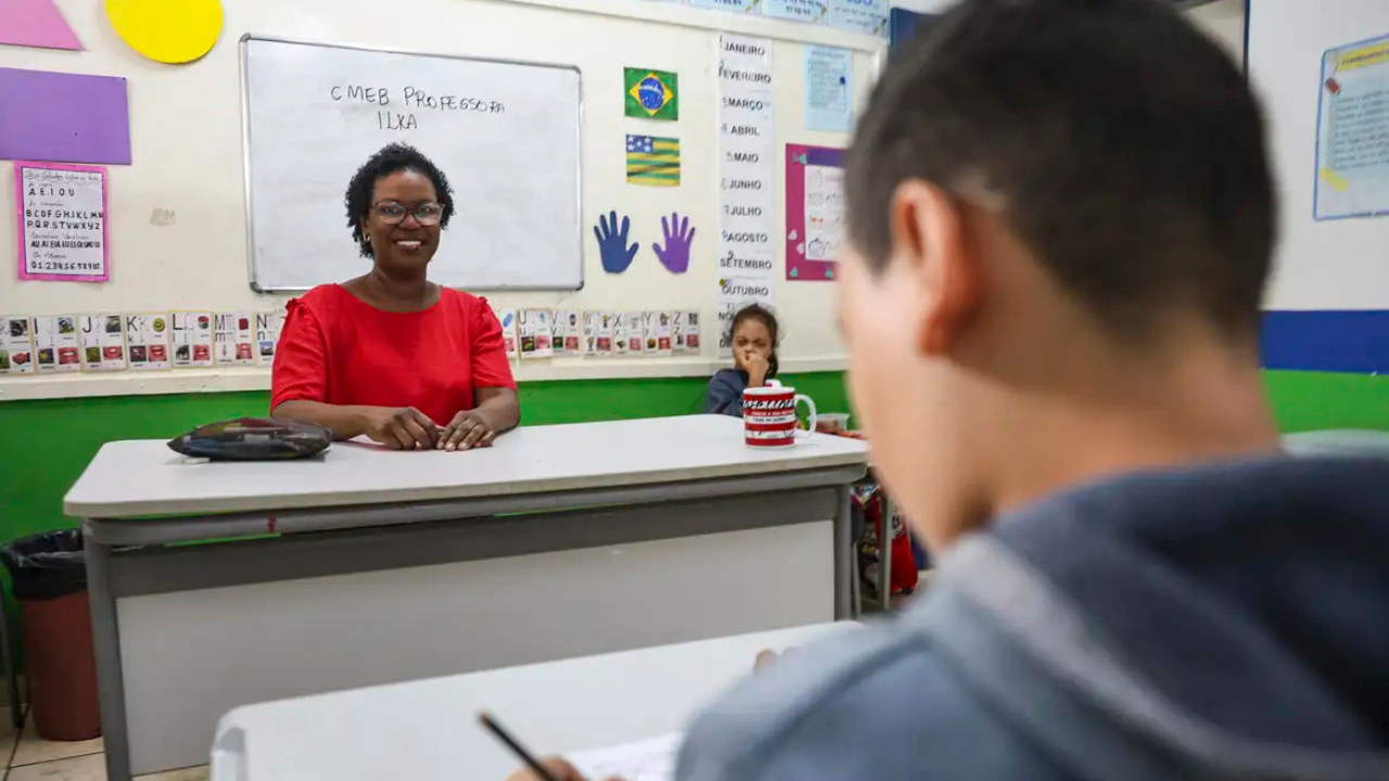 Mulher negra sentada à mesa em sala de aula com alunos Mulher negra sentada à mesa em sala de aula com alunos