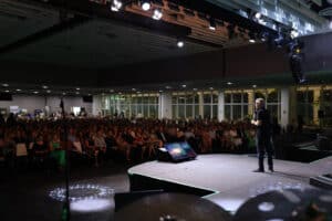 Palco de palestra da Collab Inovação com várias pessoas assistindo