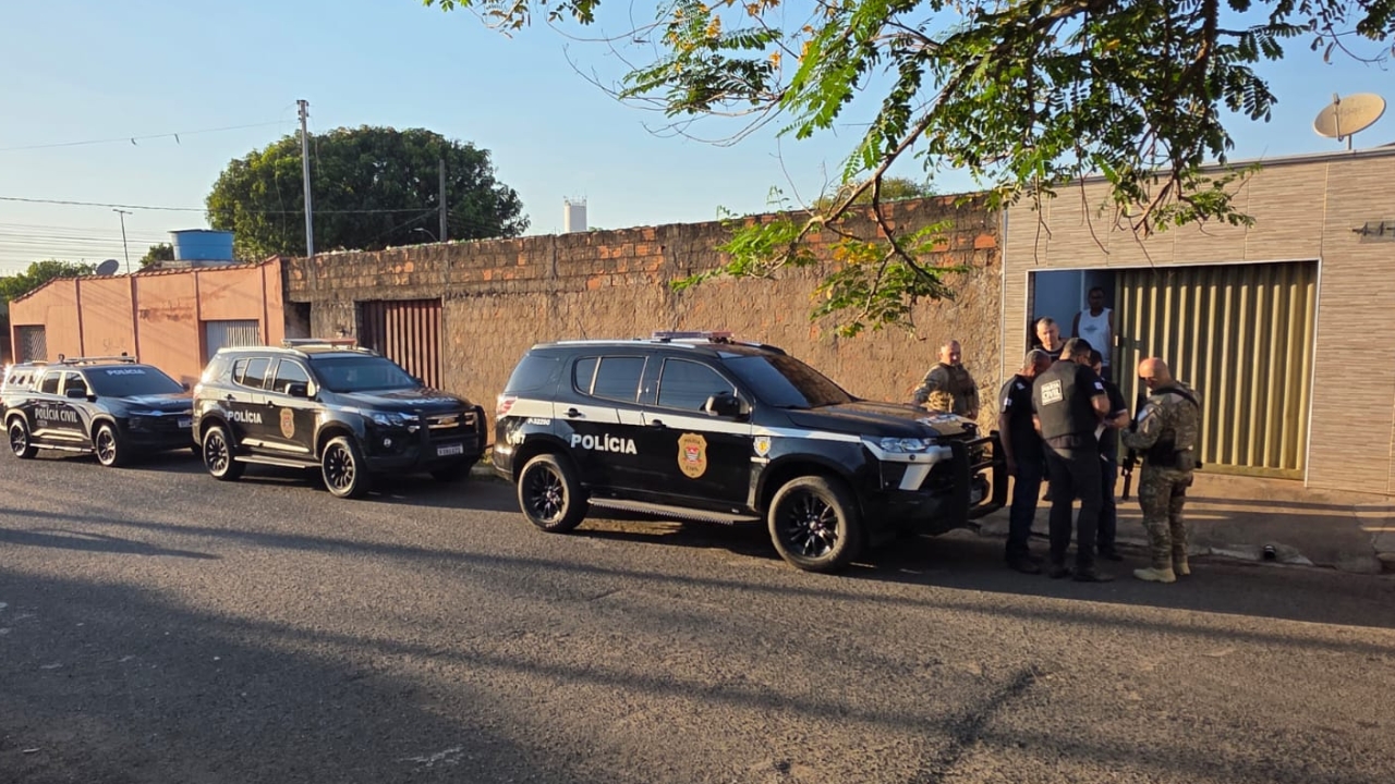 carros da polícia civil estacionado na rua e policiais em pé na frente de uma casa