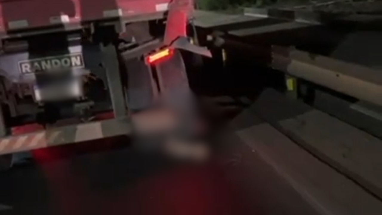 Imagem da parte traseira de um caminhão, com uma parte borrada, onde está a vítima Imagem da parte traseira de um caminhão, com uma parte borrada, onde está a vítima