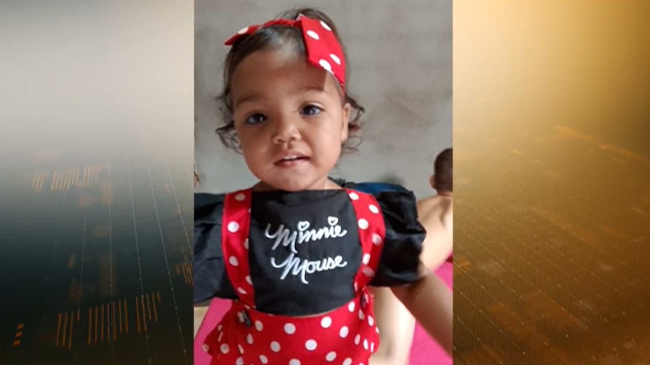 Imagem da bebê de 1 ano e 6 meses, que foi encontrada morta. A menina usa uma roupa preta com macacão vermelho pintado