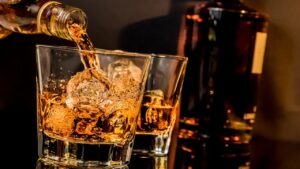 Intoxicação de metanol // Imagem de dois copos de whiskey com gelo; o primeiro sendo servido. Ao fundo uma garrafa da bebida