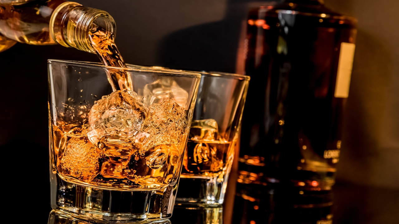 Intoxicação de metanol // Imagem de dois copos de whiskey com gelo; o primeiro sendo servido. Ao fundo uma garrafa da bebida