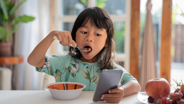 criança comendo enquanto mexe no celular
